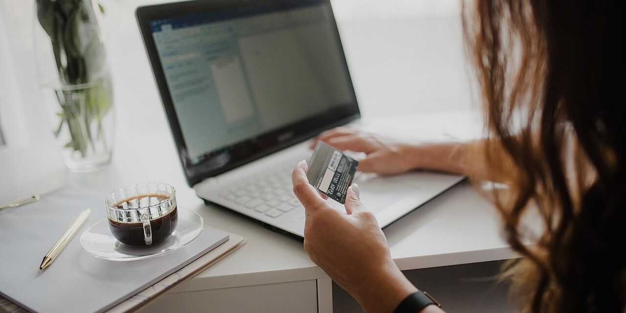 Woman holding a payment card while working on a laptop