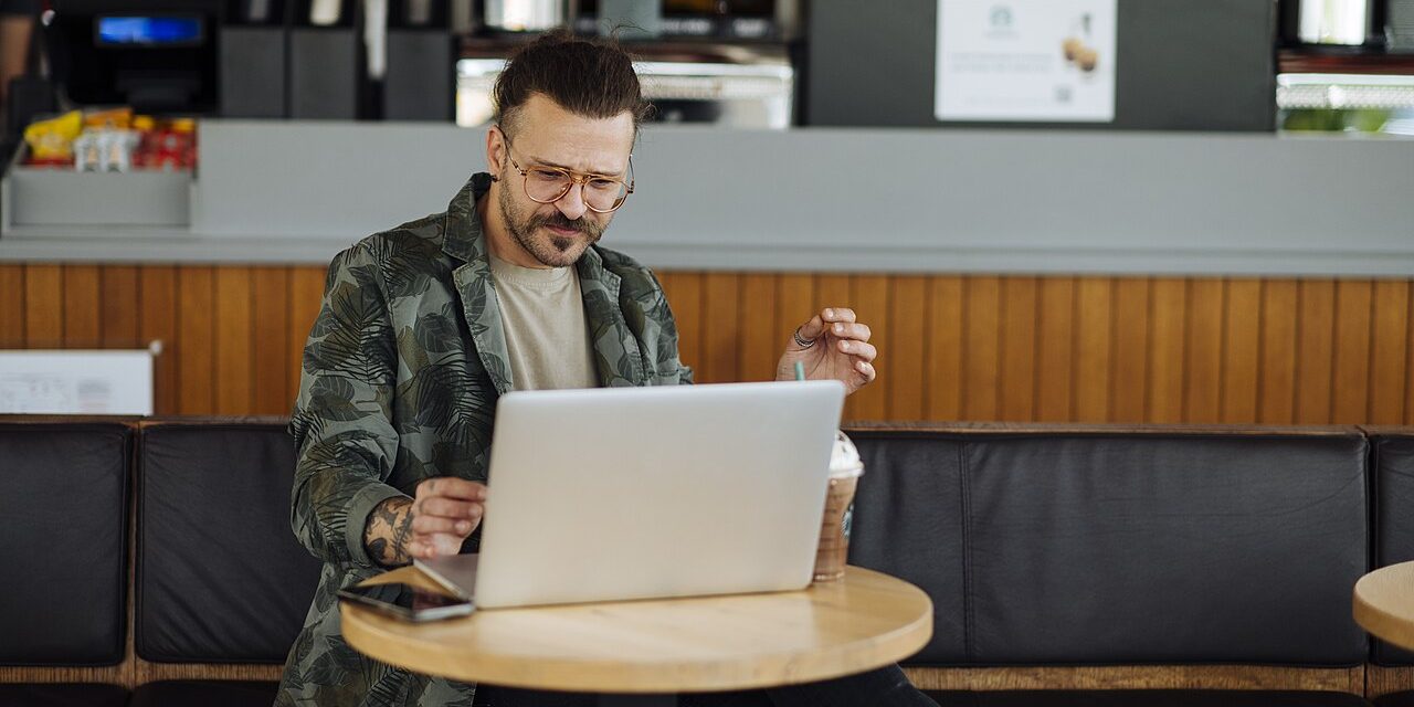 Man working on cloud apps on a laptop in a cafe