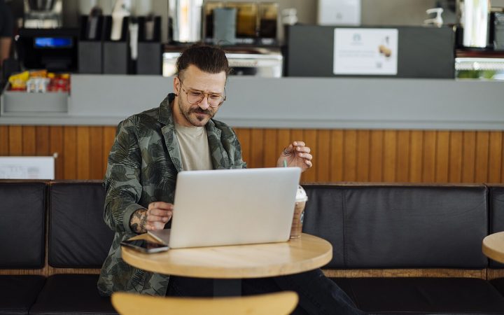Man working on cloud apps on a laptop in a cafe