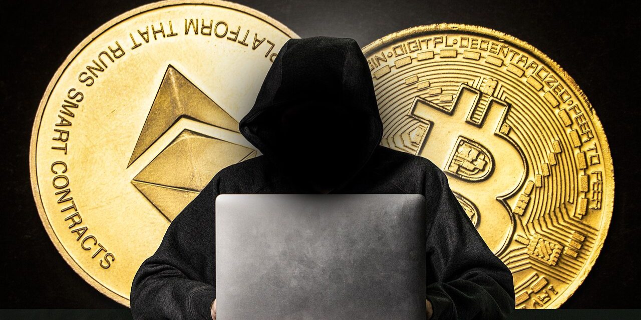 Hooded figure behind a laptop representing a cyber attacker
