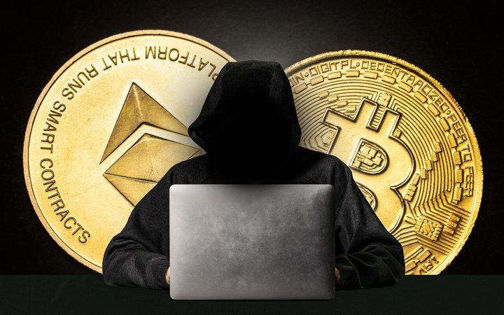 Hooded figure behind a laptop representing a cyber attacker