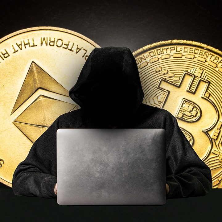 Hooded figure behind a laptop representing a cyber attacker