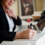 Business professional taking notes next to a laptop